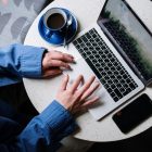 person in blue denim jeans using macbook pro beside white ceramic mug on white table
